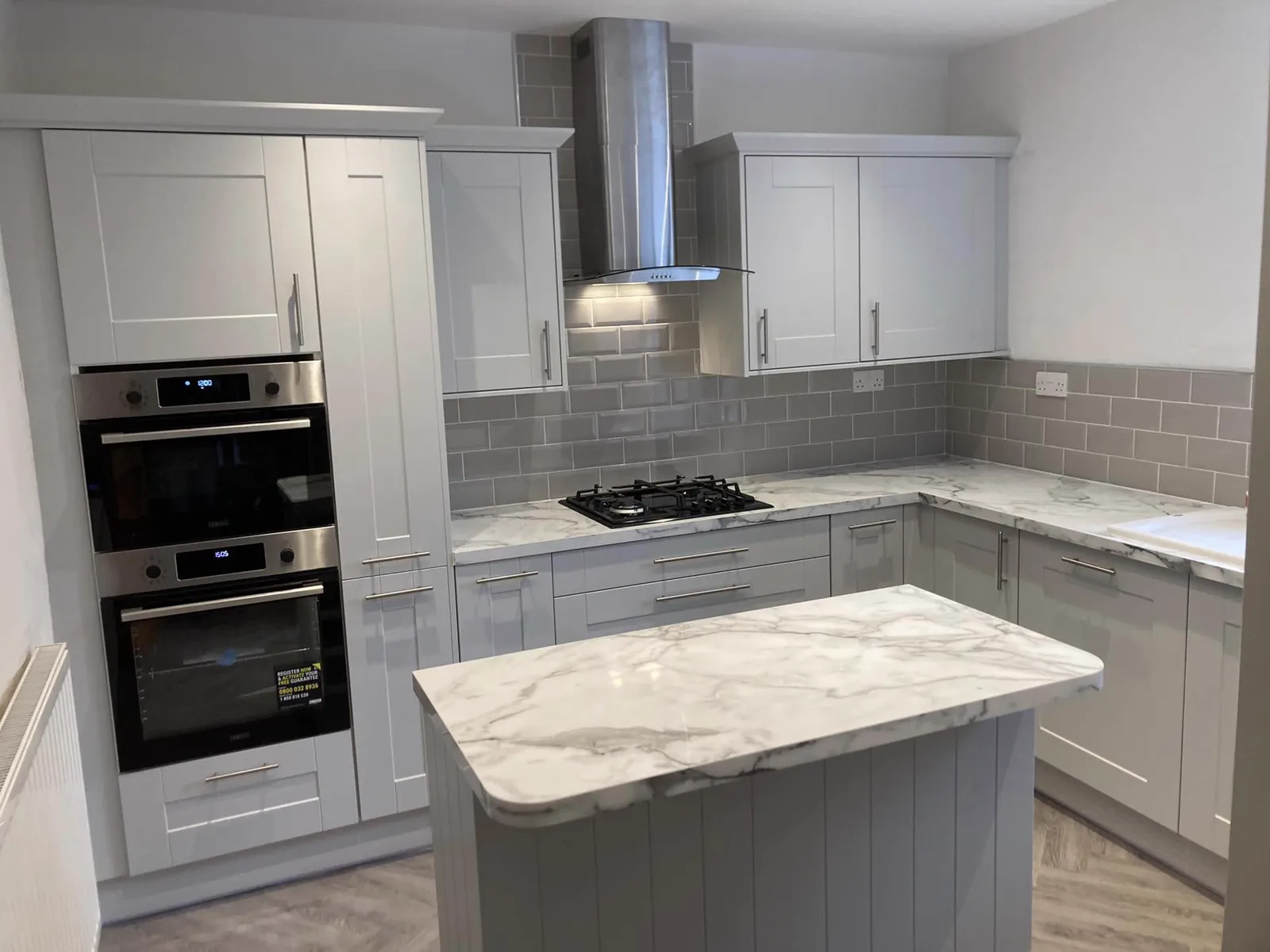 Finished kitchen renovation with white cabinetry, grey tiled splashback and marble island